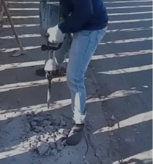 Homem quebrando calçada com martelete em obra